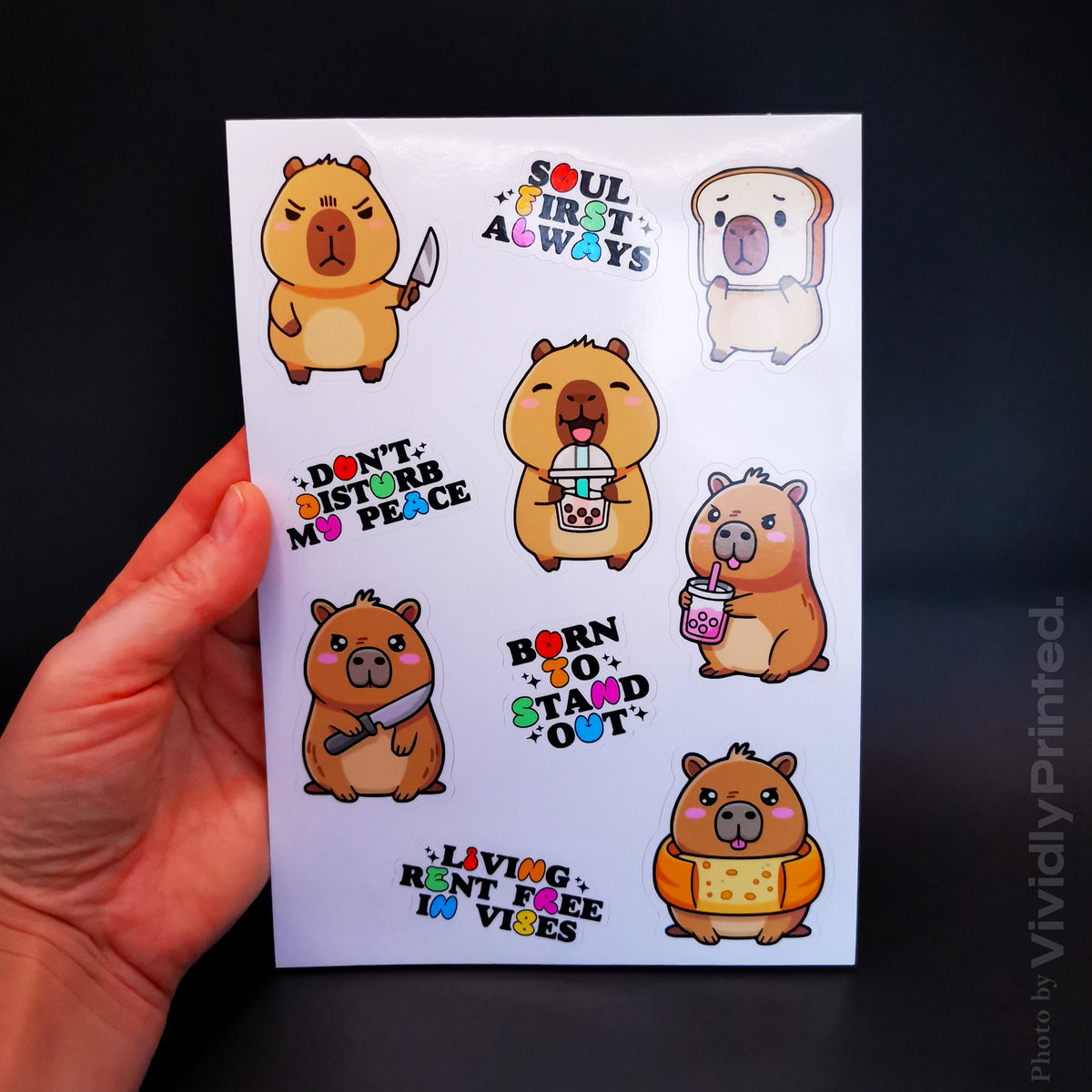 A hand holding a sticker sheet with cartoon capybara designs