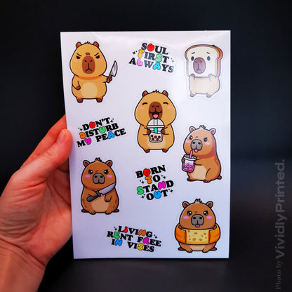 A hand holding a sticker sheet with cartoon capybara designs