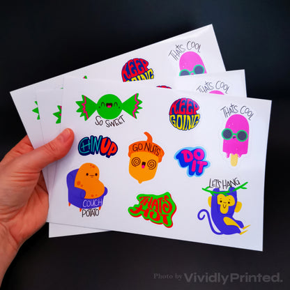 A hand holding sticker sheets with colourful sweets and slogan designs