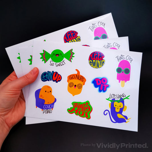 A hand holding sticker sheets with colourful sweets and slogan designs